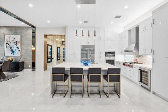 kitchen with a center island, hanging light fixtures, wine cooler, built in appliances, and wall chimney exhaust hood