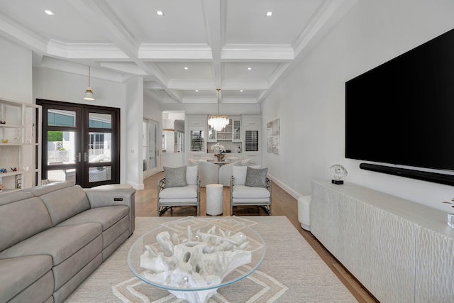 living room featuring french doors, light wood-type flooring, a notable chandelier, beam ceiling, and coffered ceiling