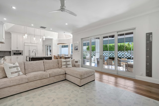 living room featuring ceiling fan with notable chandelier, ornamental molding, and light hardwood / wood-style flooring