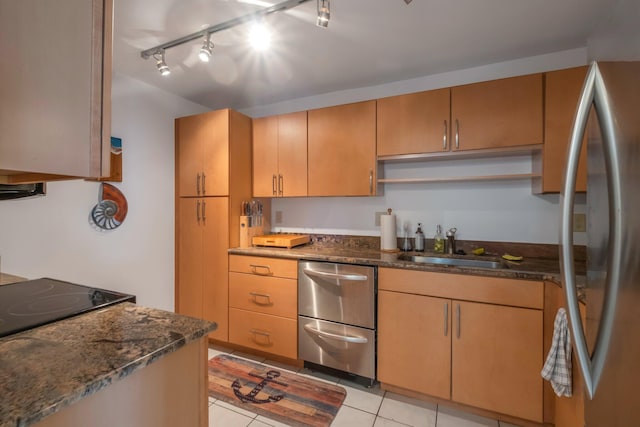 kitchen with stainless steel appliances, dark stone counters, sink, rail lighting, and light tile patterned floors