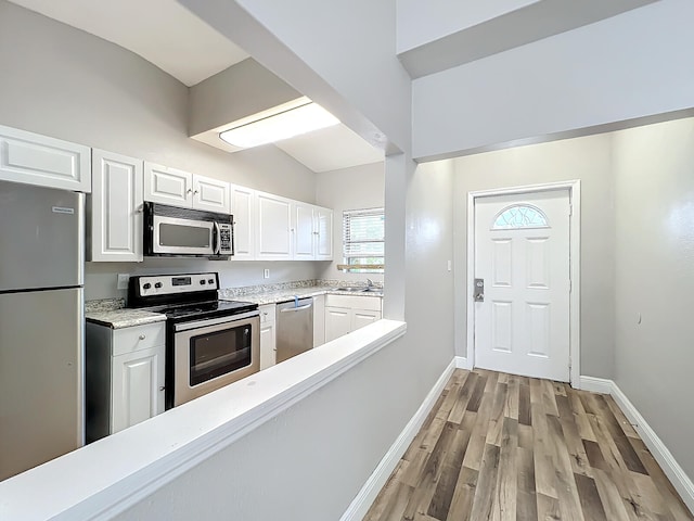 kitchen with stainless steel appliances, light wood-type flooring, white cabinetry, sink, and vaulted ceiling