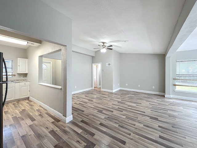 unfurnished living room with a wealth of natural light, ceiling fan, vaulted ceiling, and light hardwood / wood-style flooring