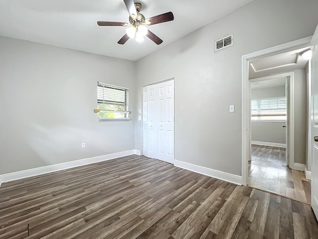 unfurnished bedroom with dark wood-type flooring, ceiling fan, multiple windows, and a closet