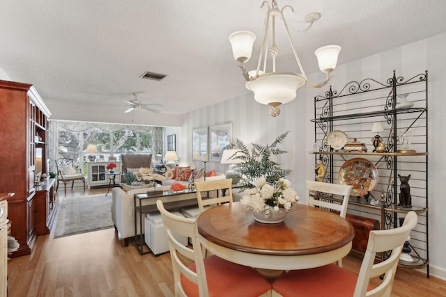 dining space with ceiling fan with notable chandelier, a textured ceiling, and light wood-type flooring