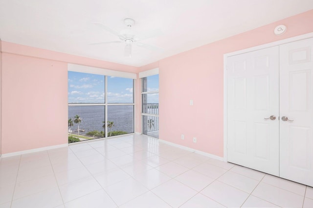 spare room with light tile patterned flooring, ceiling fan, and a water view