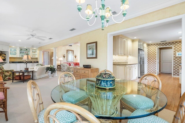 dining area with ornate columns, ceiling fan with notable chandelier, ornamental molding, and light hardwood / wood-style flooring