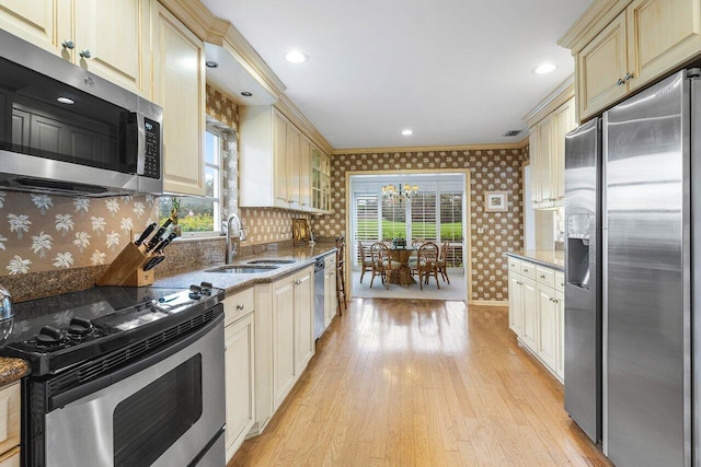 kitchen featuring stainless steel appliances, light hardwood / wood-style floors, sink, cream cabinets, and ornamental molding