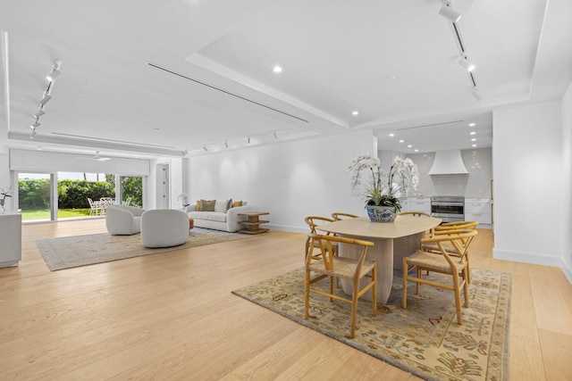 dining room with a raised ceiling, track lighting, and light hardwood / wood-style flooring