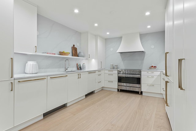 kitchen with custom exhaust hood, stainless steel electric stove, light countertops, white cabinets, and a sink