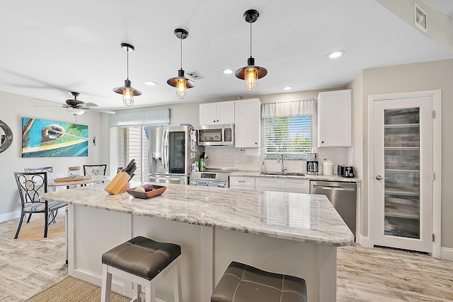 18352 Flagship Cir, Jupiter, FL 33458 - kitchen featuring appliances with stainless steel finishes, a kitchen breakfast bar, white cabinetry, light wood finished floors, and decorative backsplash