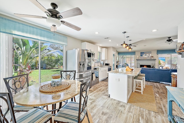 kitchen featuring appliances with stainless steel finishes, a brick fireplace, light stone counters, light hardwood / wood-style flooring, and white cabinetry