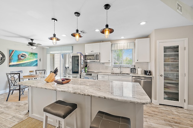 kitchen with pendant lighting, sink, light stone counters, white cabinetry, and stainless steel appliances