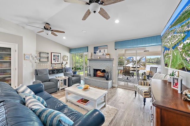 living room featuring ceiling fan, light hardwood / wood-style floors, lofted ceiling, and a brick fireplace