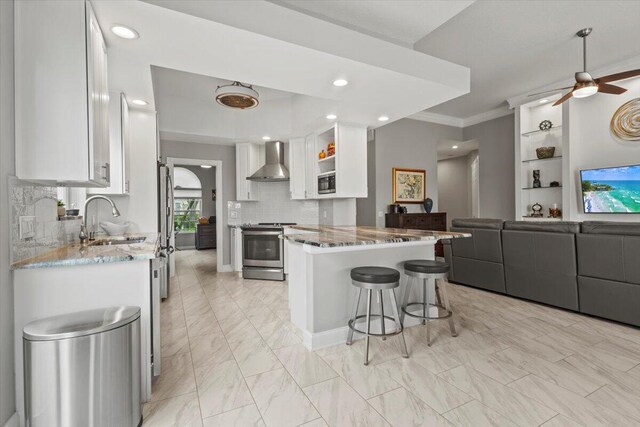 kitchen with stainless steel appliances, sink, backsplash, white cabinets, and wall chimney range hood