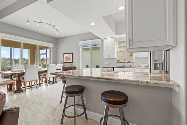 kitchen with white cabinetry, kitchen peninsula, a kitchen breakfast bar, light stone countertops, and backsplash