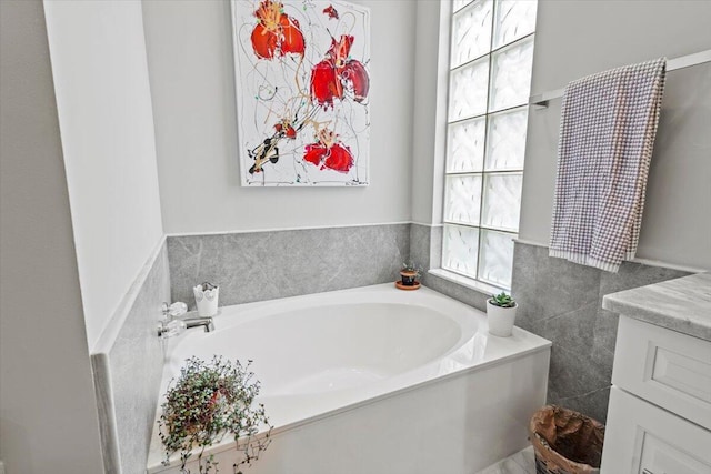 bathroom with tile walls, vanity, a healthy amount of sunlight, and a bathing tub