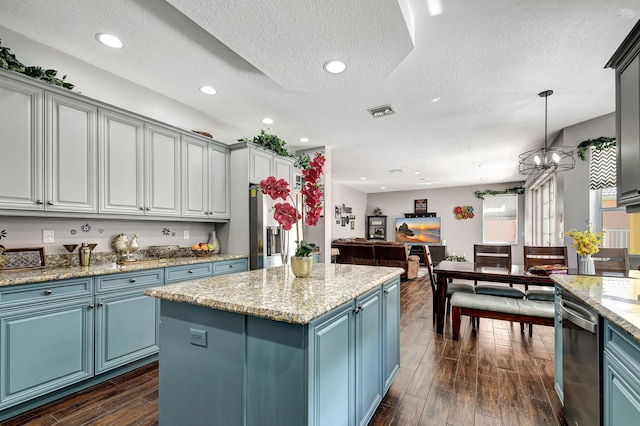 kitchen with stainless steel appliances, dark hardwood / wood-style floors, a textured ceiling, decorative light fixtures, and a kitchen island