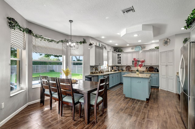 kitchen featuring stainless steel fridge, a kitchen island, a textured ceiling, pendant lighting, and dark wood-type flooring