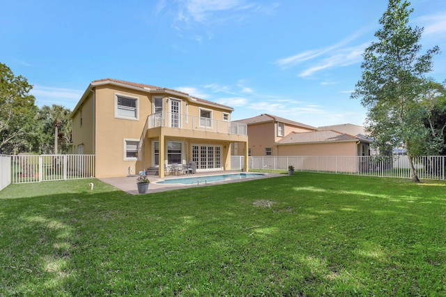 rear view of property featuring a fenced in pool, a patio, a balcony, and a yard