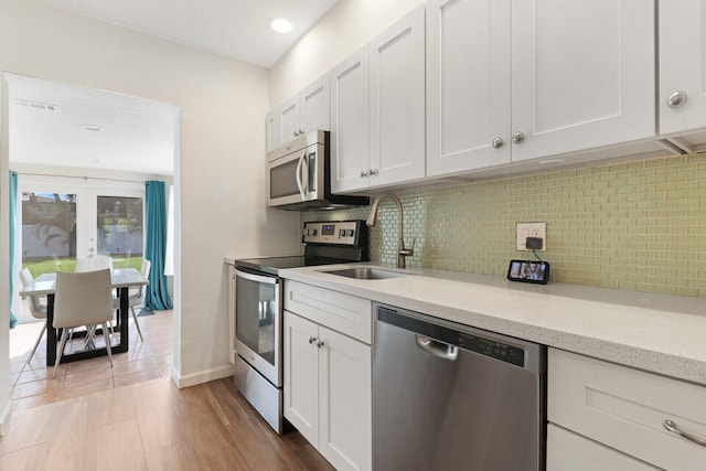 kitchen with sink, white cabinetry, stainless steel appliances, hardwood / wood-style flooring, and decorative backsplash