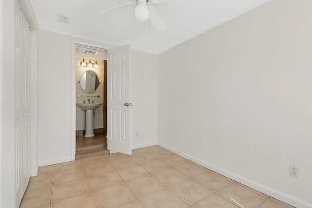 unfurnished bedroom with ensuite bathroom, sink, light tile patterned floors, and ceiling fan