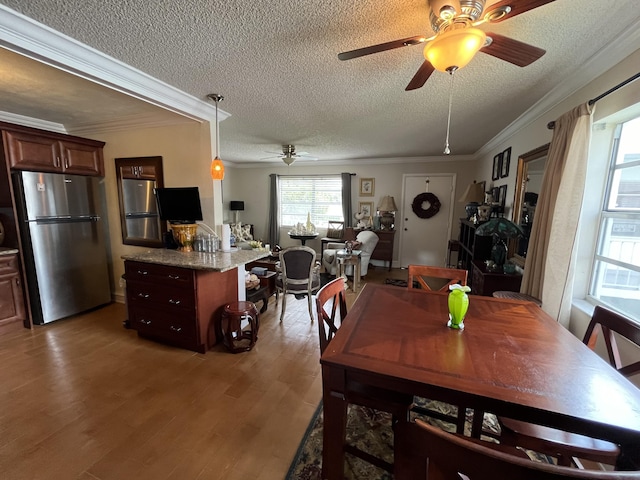 dining area featuring a textured ceiling, ceiling fan, light wood-style flooring, and crown molding