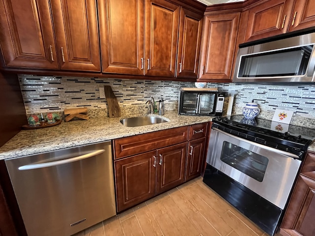 kitchen with decorative backsplash, appliances with stainless steel finishes, light stone countertops, light wood-style floors, and a sink