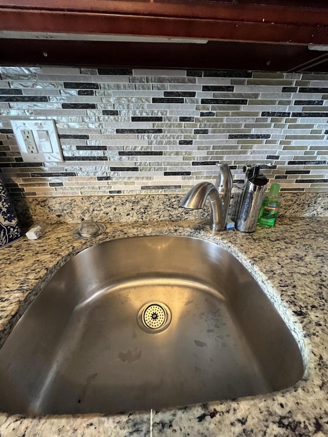 interior details featuring light stone counters, a sink, and decorative backsplash