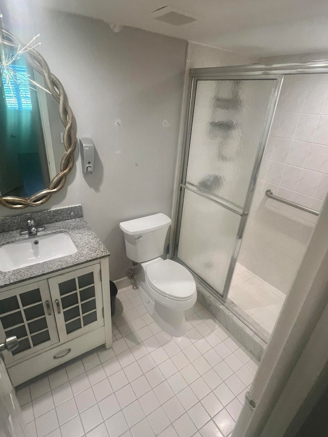 bathroom with tile patterned floors, vanity, a shower with shower door, and toilet