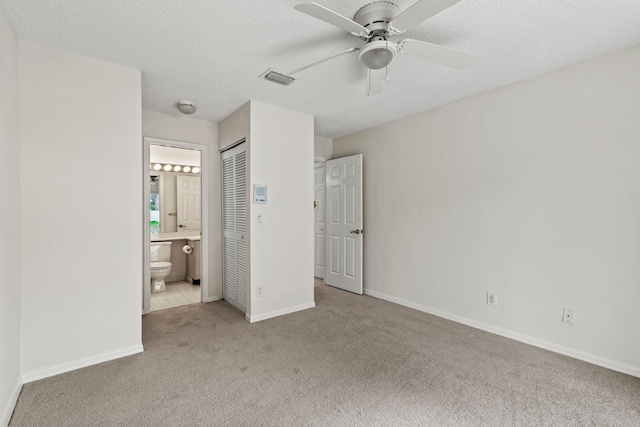 unfurnished bedroom featuring ensuite bath, light colored carpet, a textured ceiling, ceiling fan, and a closet