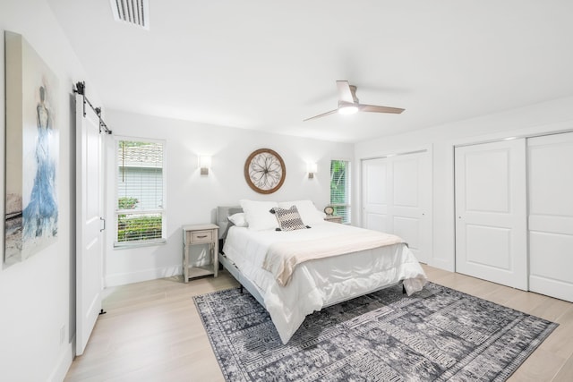 bedroom with ceiling fan, a barn door, light wood-type flooring, and two closets