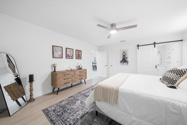 bedroom with ceiling fan, a barn door, light hardwood / wood-style floors, and a closet