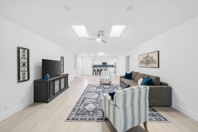 living room featuring ceiling fan, vaulted ceiling with skylight, and light hardwood / wood-style floors