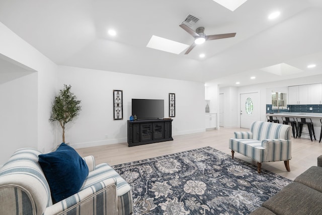 living room with ceiling fan, light hardwood / wood-style floors, and a skylight