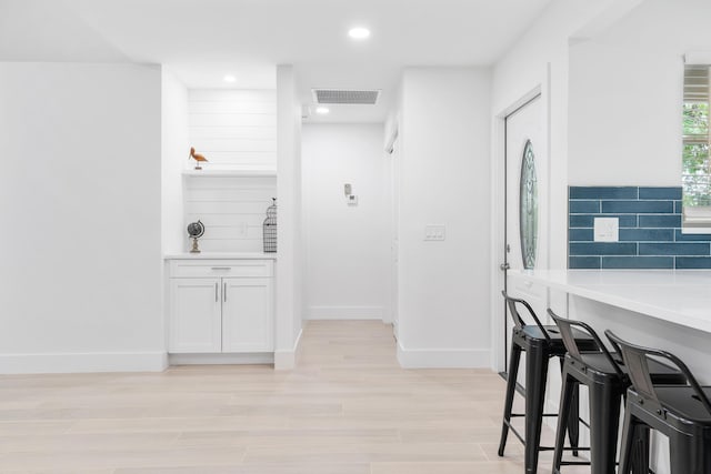 kitchen with backsplash, a breakfast bar, light hardwood / wood-style flooring, and white cabinets