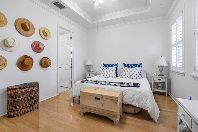 bedroom featuring ceiling fan, light wood-type flooring, crown molding, and a tray ceiling