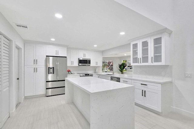 kitchen with appliances with stainless steel finishes, light stone counters, sink, a center island, and white cabinetry