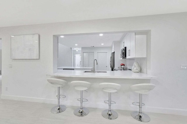 kitchen with white cabinets, sink, stainless steel fridge, kitchen peninsula, and a breakfast bar area