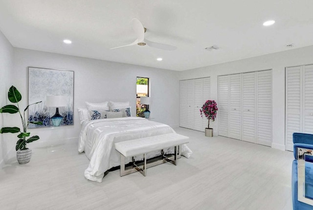 bedroom featuring ceiling fan, light hardwood / wood-style flooring, and two closets