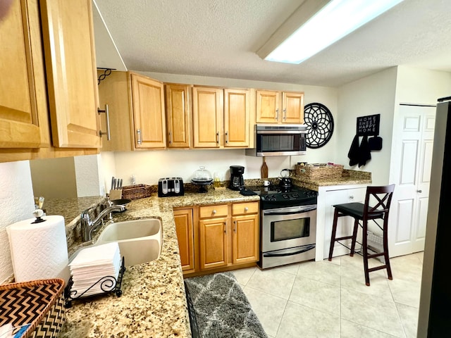 kitchen with sink, stainless steel appliances, light stone counters, a textured ceiling, and light tile patterned flooring