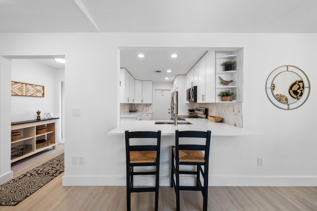 kitchen featuring kitchen peninsula, appliances with stainless steel finishes, white cabinetry, and light hardwood / wood-style flooring