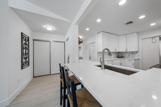 kitchen featuring sink, tasteful backsplash, light hardwood / wood-style flooring, a kitchen bar, and white cabinets