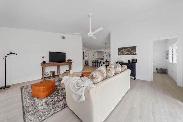 living room featuring ceiling fan with notable chandelier, lofted ceiling, and light hardwood / wood-style flooring