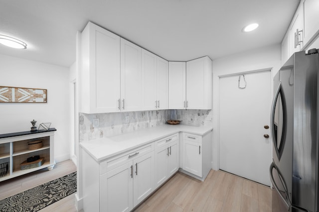 kitchen with white cabinets, light hardwood / wood-style floors, stainless steel refrigerator, and tasteful backsplash