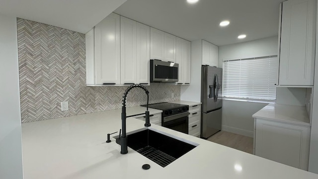 kitchen featuring appliances with stainless steel finishes, sink, light wood-type flooring, white cabinetry, and decorative backsplash