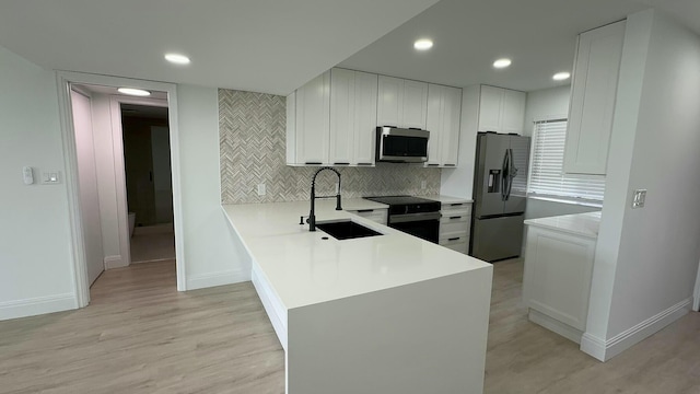 kitchen with appliances with stainless steel finishes, sink, light wood-type flooring, kitchen peninsula, and white cabinets