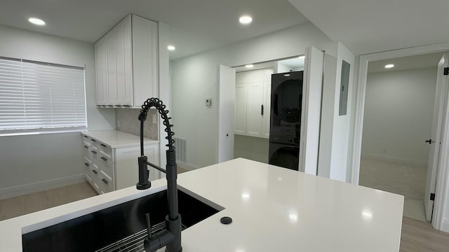 kitchen featuring stacked washing maching and dryer, backsplash, sink, light wood-type flooring, and white cabinetry