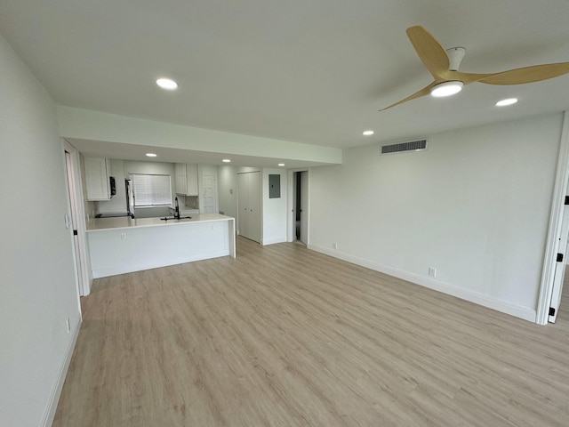 unfurnished living room with light hardwood / wood-style floors, electric panel, sink, and ceiling fan