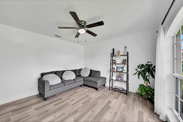 living room with a textured ceiling, light wood-type flooring, a wealth of natural light, and ceiling fan