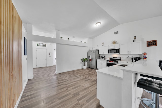 kitchen with stainless steel appliances, sink, vaulted ceiling, white cabinets, and kitchen peninsula